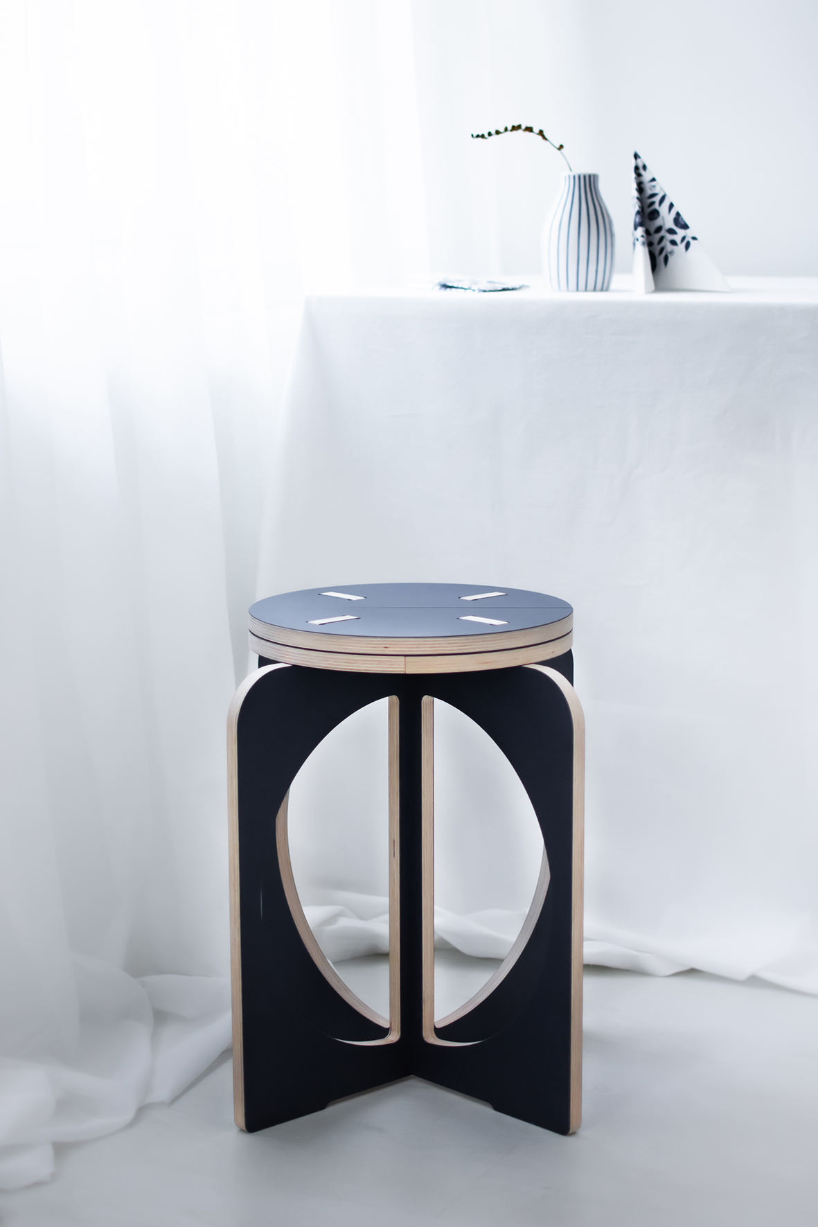 Opilion blue design stool. In the background, a white-blue pot with one branch. Next to the pot is a napkin.  