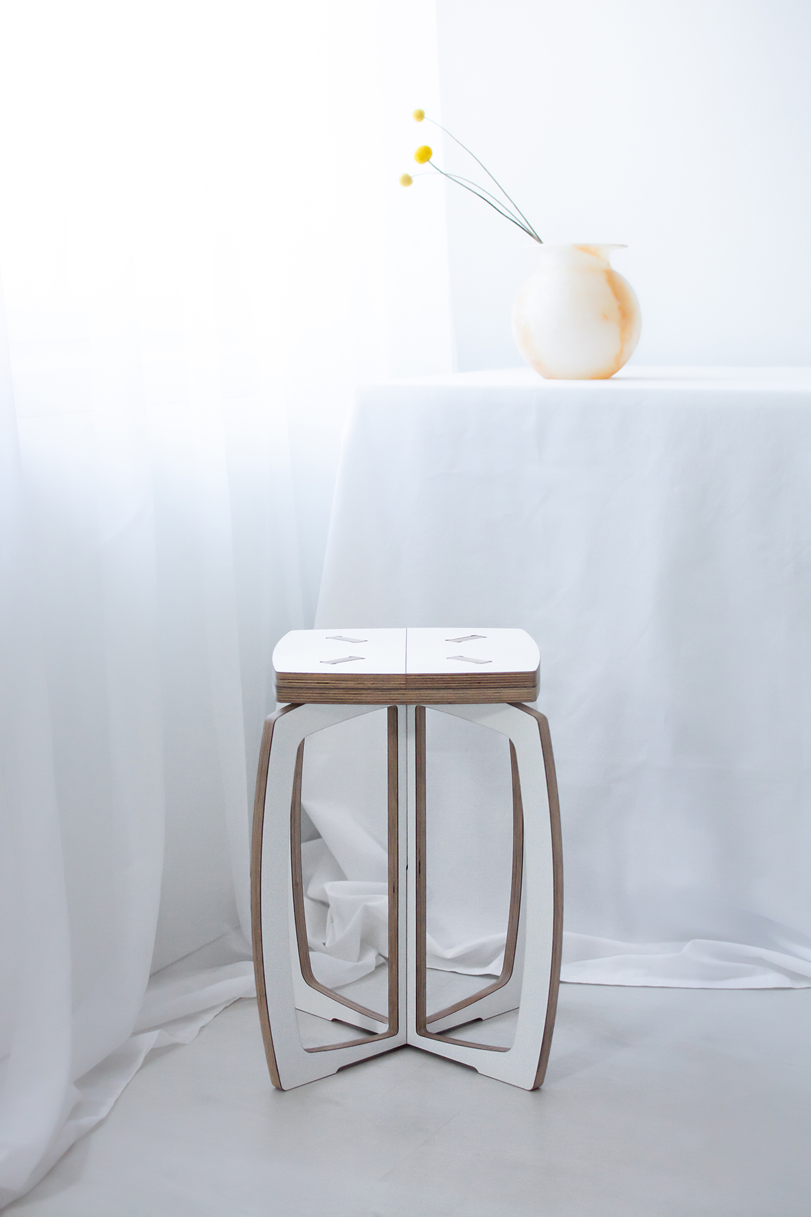 Opilion white design stool. In the background is a white-orange pot with three orange flowers. 